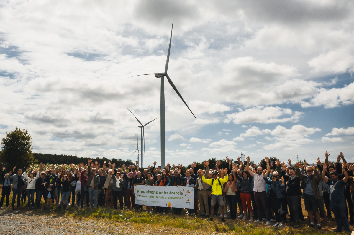 Photo de groupe des actionnaires citoyens du parc de l'Hyrôme levant les bras en l'air devant les éoliennes.